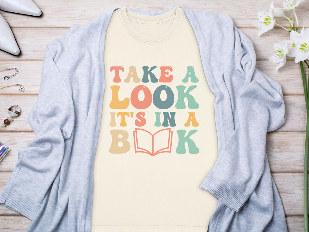 T-shirt with "TAKE A LOOK IT'S IN A BOOK" text and an open book graphic.