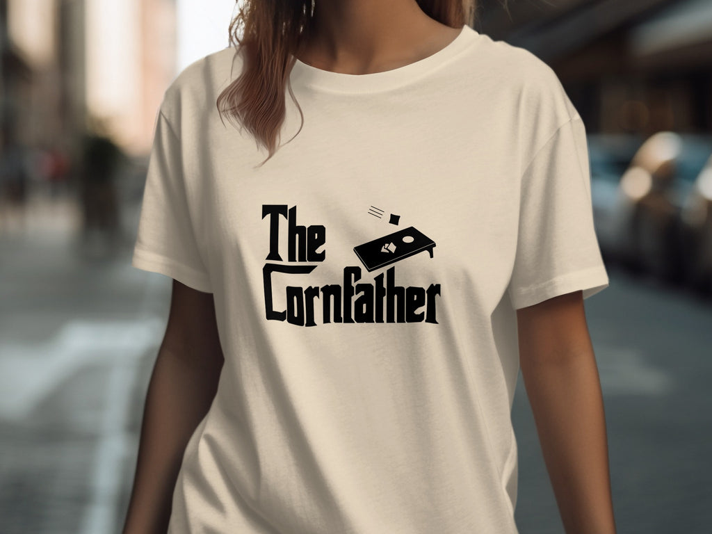 Light beige t-shirt with black text: "The Cornfather" and a cornhole board graphic.