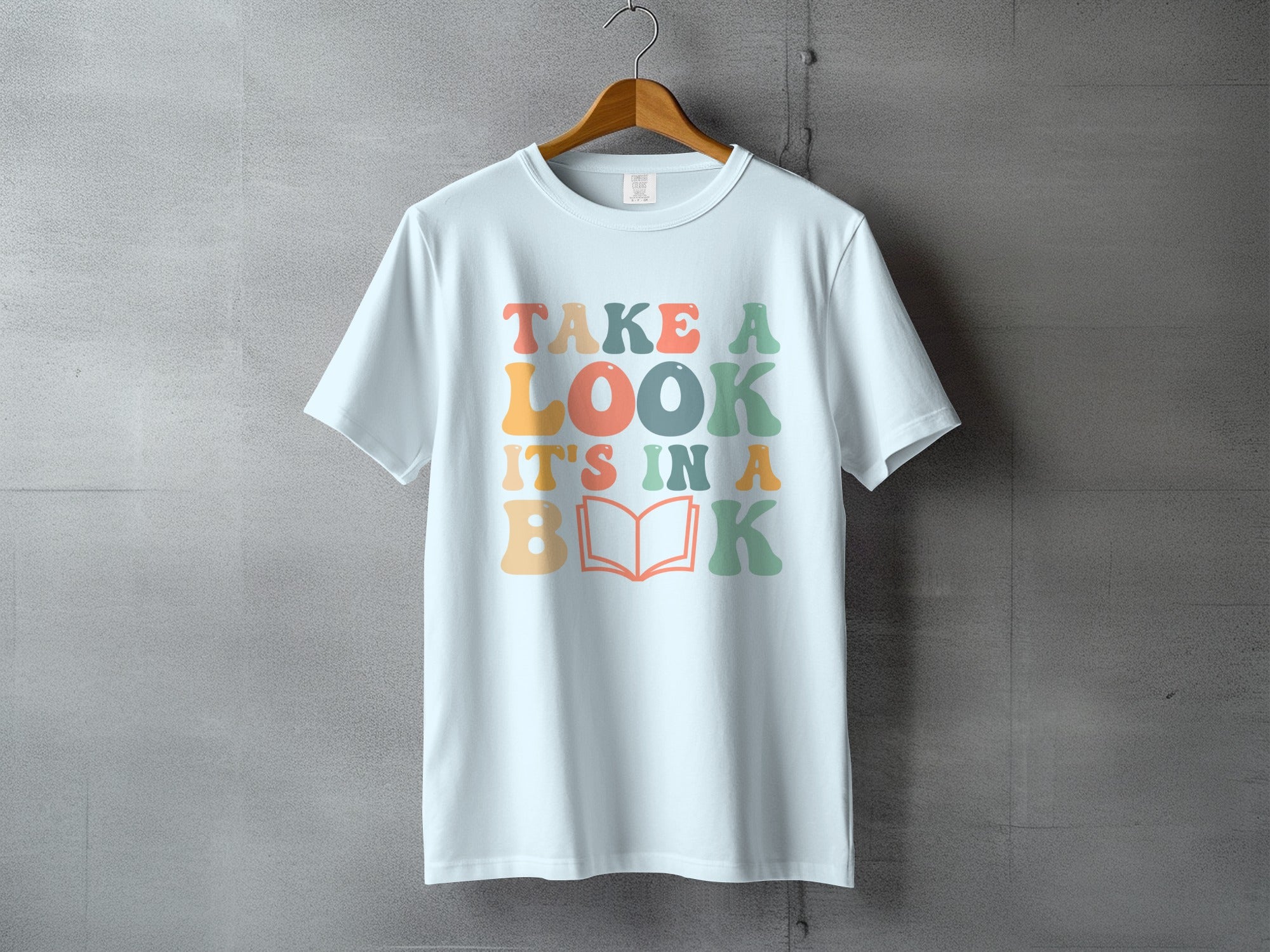 White t-shirt with colorful text "Take a Look, It's In a Book" and an open book graphic.
