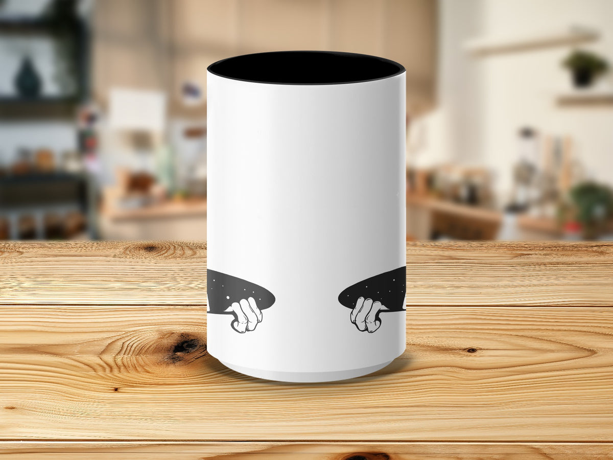 White mug with black inner rim and cutout showing hands holding starry space.