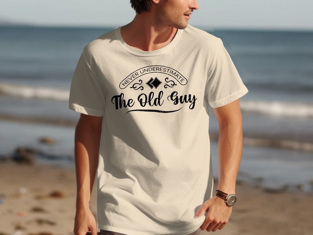 Cream t-shirt with "Never Underestimate The Old Guy" text on the front.
