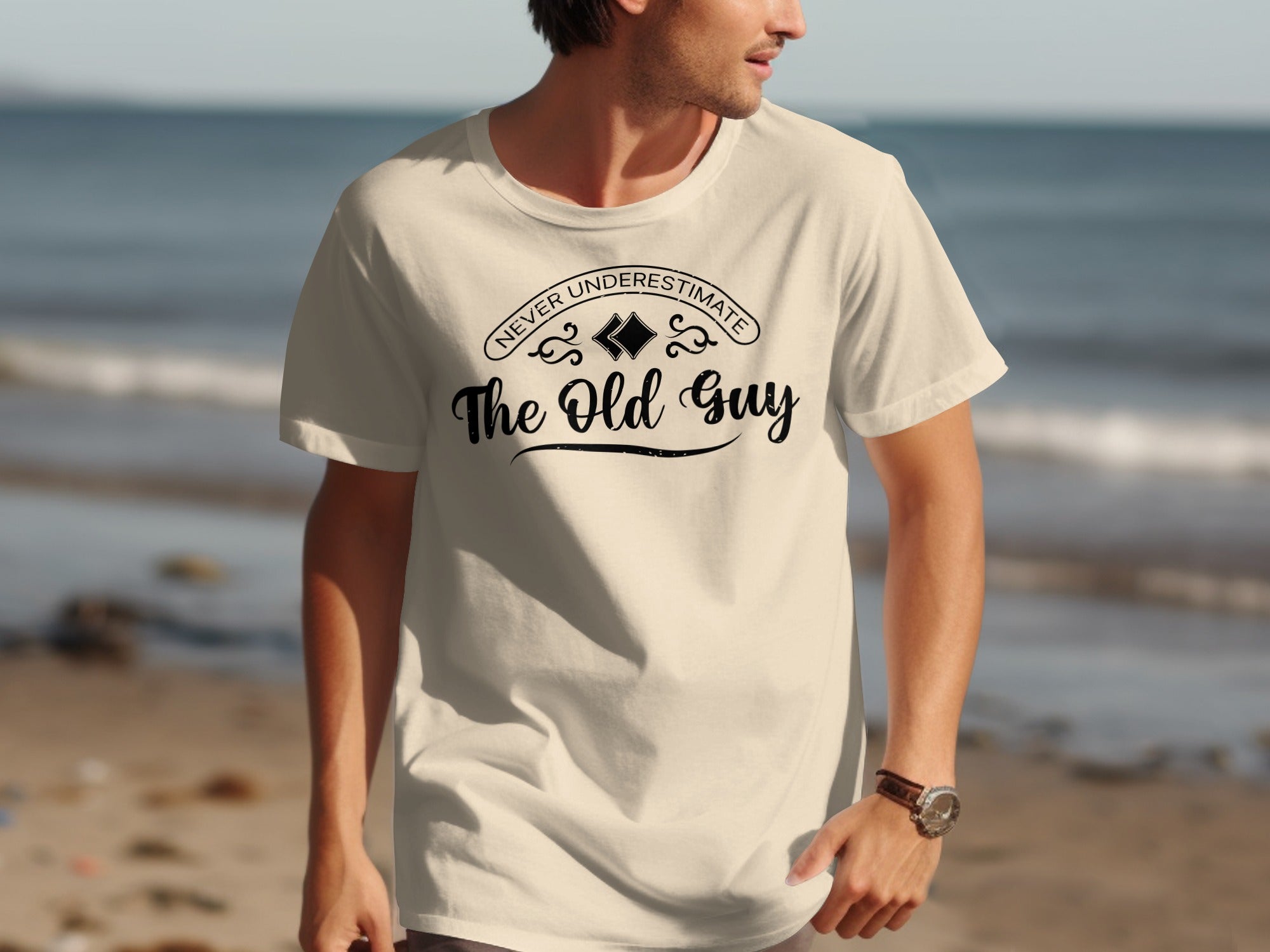Cream t-shirt with "Never Underestimate The Old Guy" text on the front.
