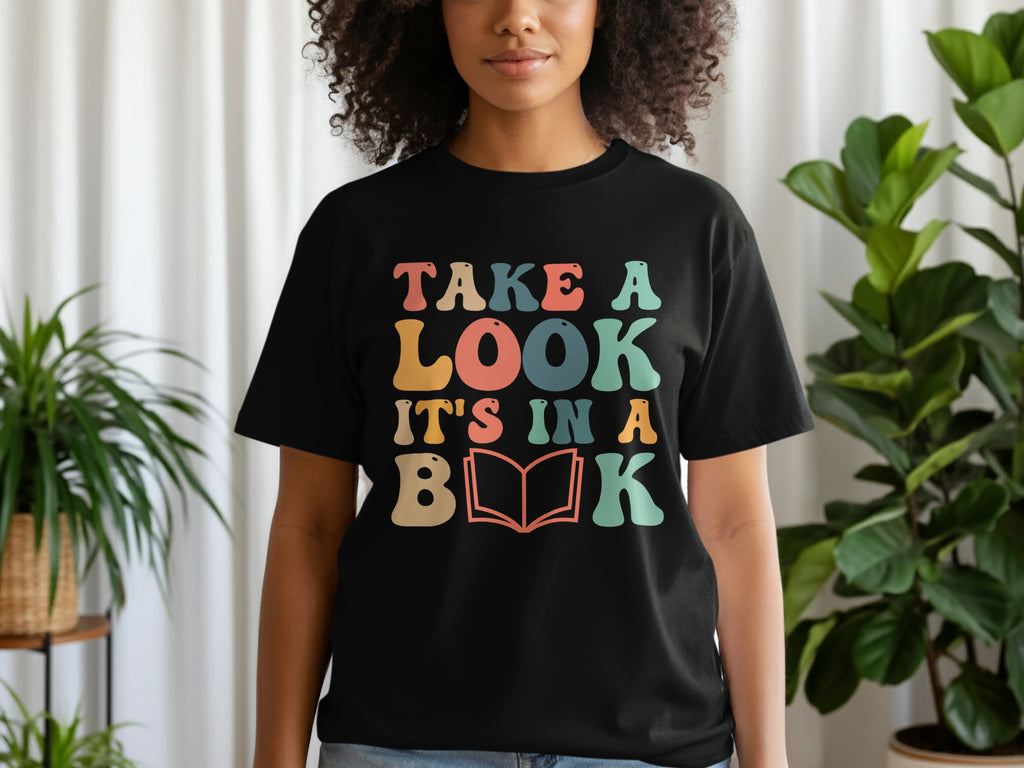 Black t-shirt with retro-style text "TAKE A LOOK IT'S IN A BOOK" and an open book icon.