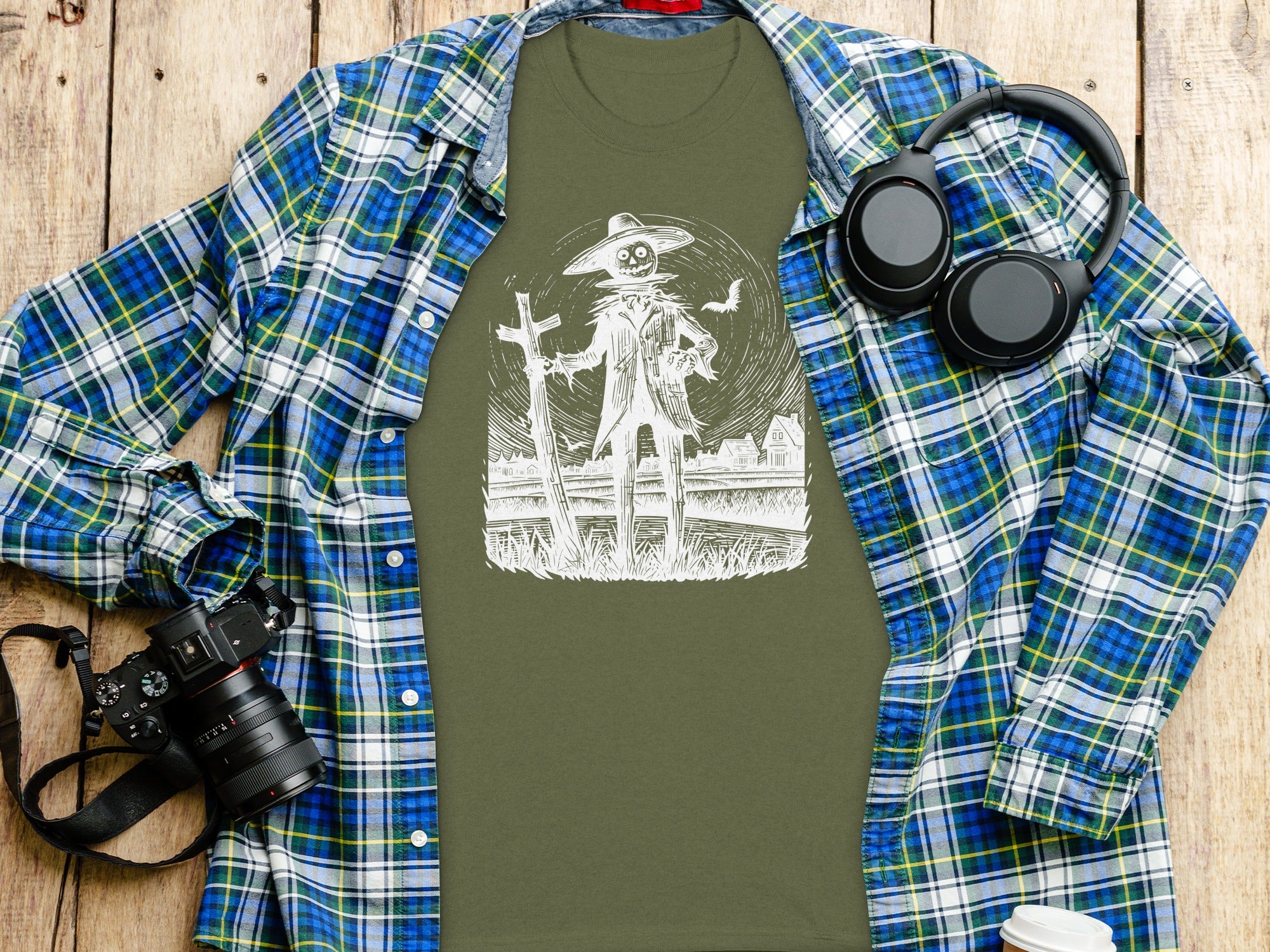 Olive green t-shirt with a white scarecrow graphic, over a blue and green plaid shirt.