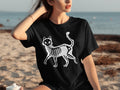 Black t-shirt with white skeleton cat graphic on beach background.