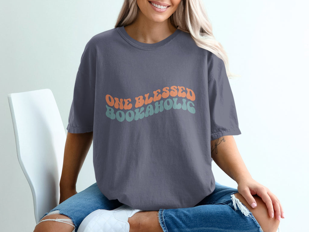 T-shirt with text "ONE BLESSED BOOKAHOLIC" in wavy orange and teal.