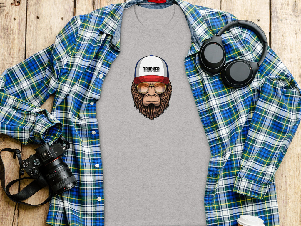 T-shirt with Bigfoot trucker graphic on wood; plaid shirt, headphones, camera