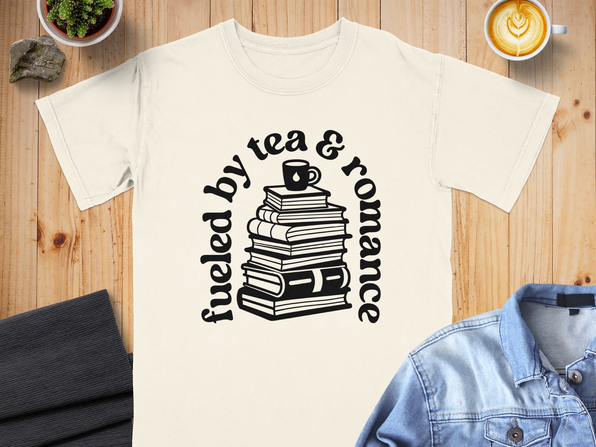 Cream t-shirt with black text "fueled by tea & romance" and stack of books graphic.