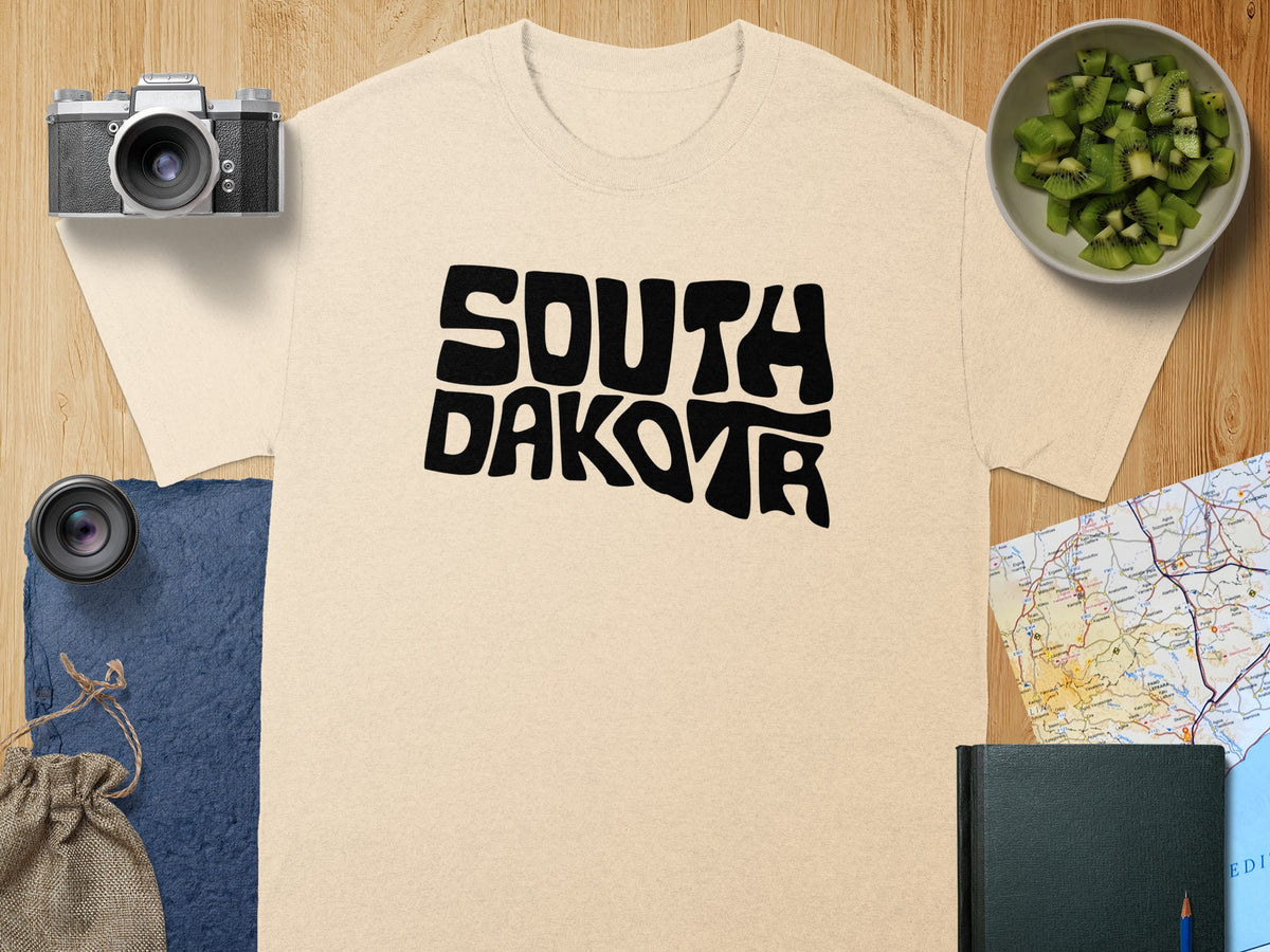 Beige t-shirt with black "South Dakota" text and travel-themed flat lay.