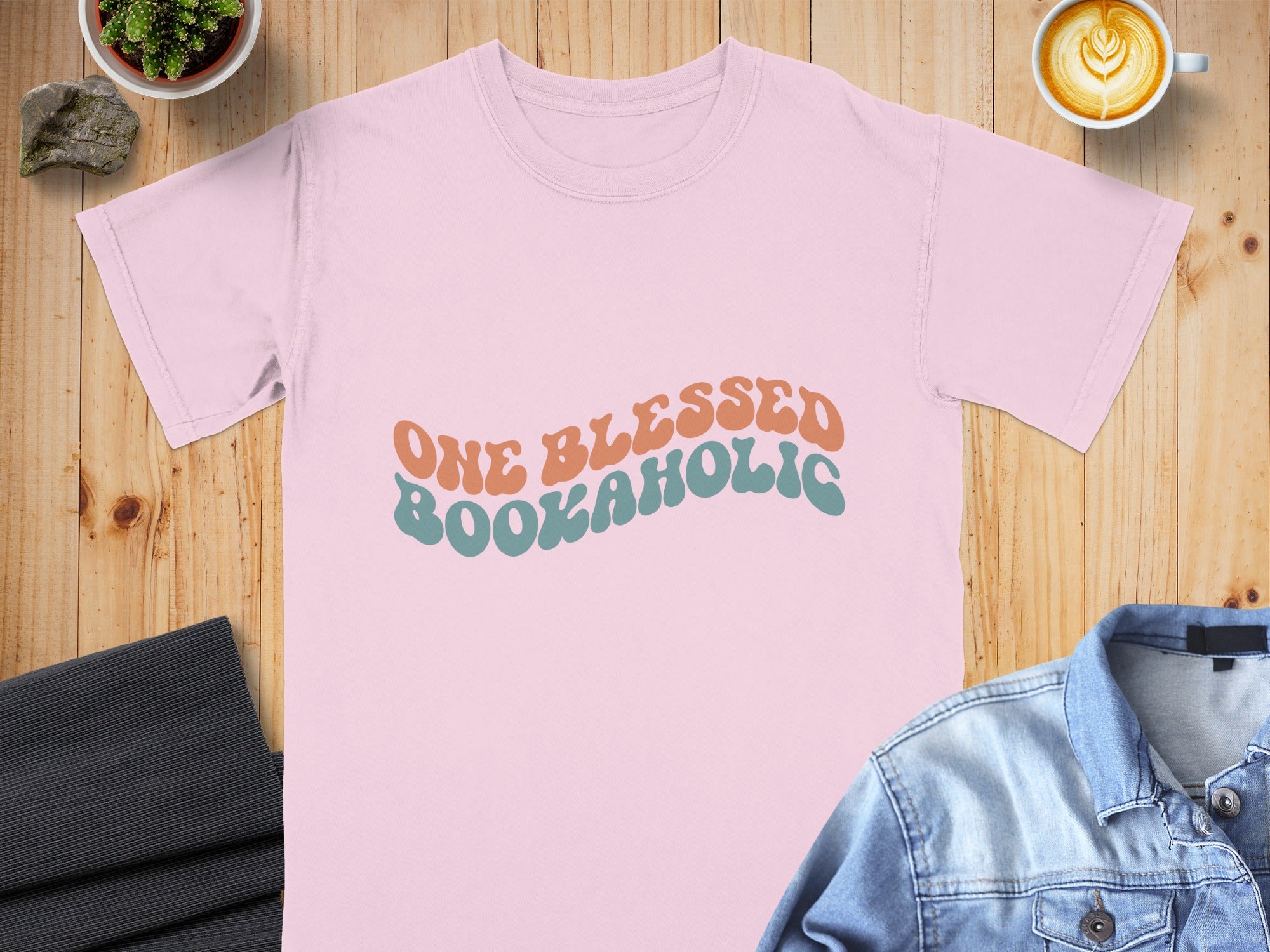 Pink t-shirt with "ONE BLESSED BOOKAHOLIC" text in wavy retro font.
