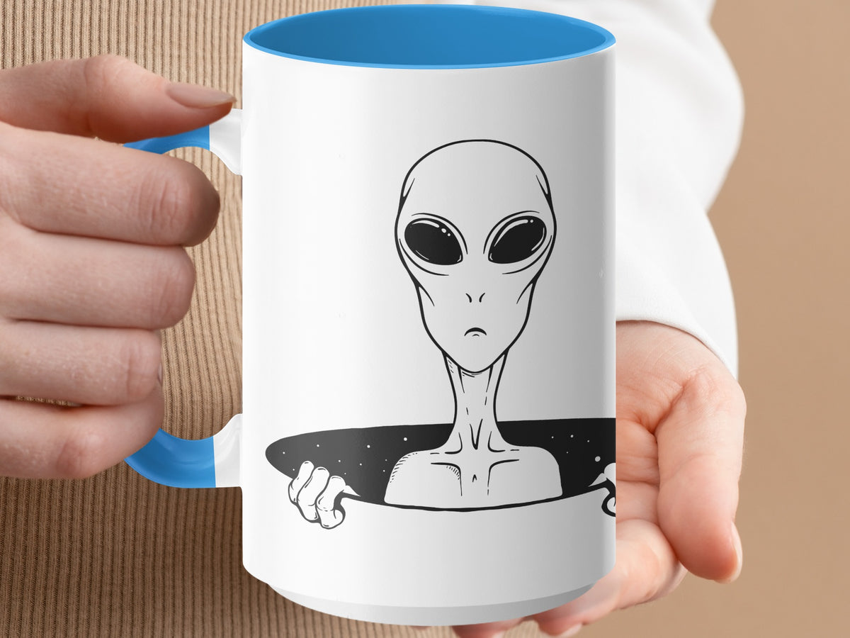 White mug with blue rim featuring a black line drawing of an alien emerging from a starry black hole.