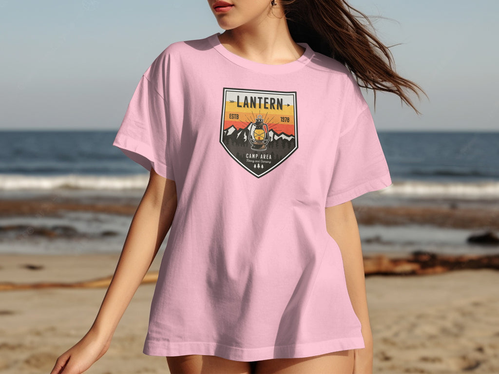 Pink t-shirt with a crest logo featuring a lantern, mountains, and text.
