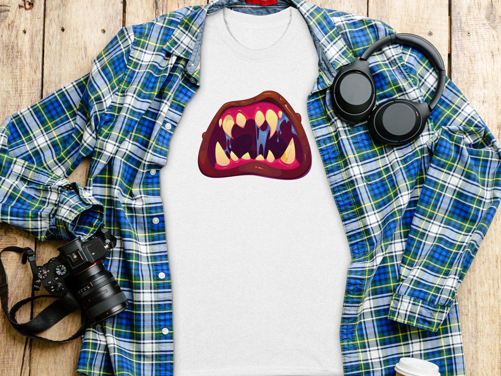 White t-shirt with a graphic of cartoon monster teeth and drool, next to a plaid shirt.