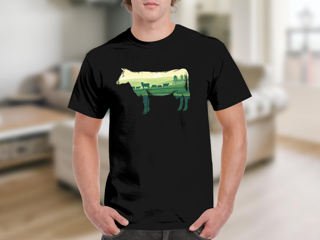 Black t-shirt with a cow silhouette filled with a farm landscape and grazing cattle.