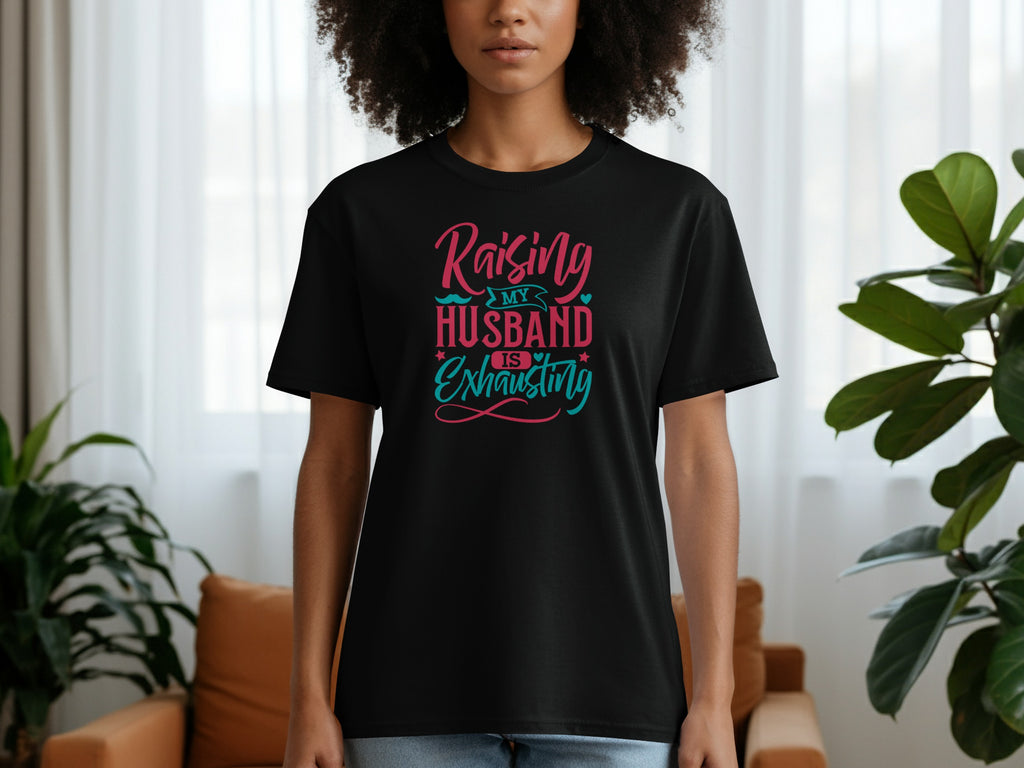 Black t-shirt with pink and teal text that reads "Raising MY HUSBAND IS Exhausting".