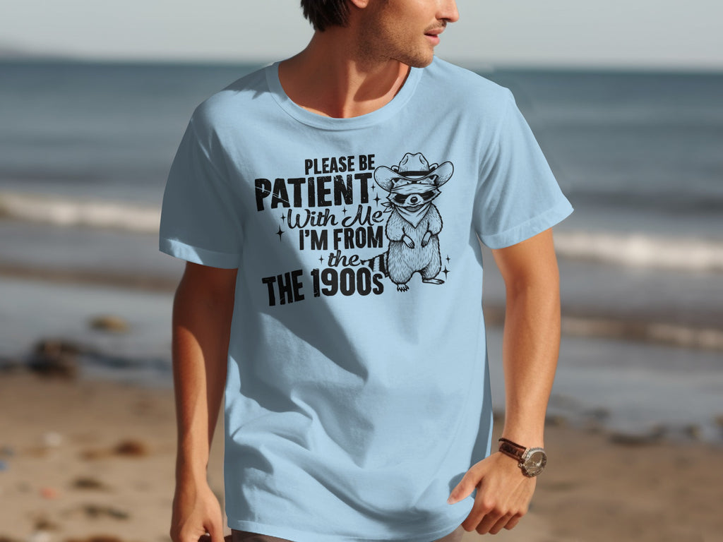 Light blue t-shirt with raccoon wearing cowboy hat and sunglasses, text "Please be patient with me I'm from the 1900s".