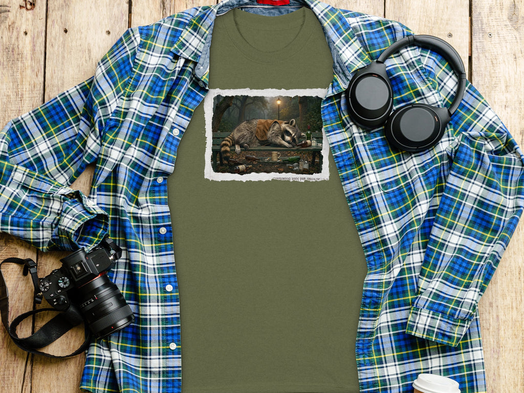 Olive green t-shirt with a distressed graphic of a raccoon sleeping on a park bench surrounded by bottles.