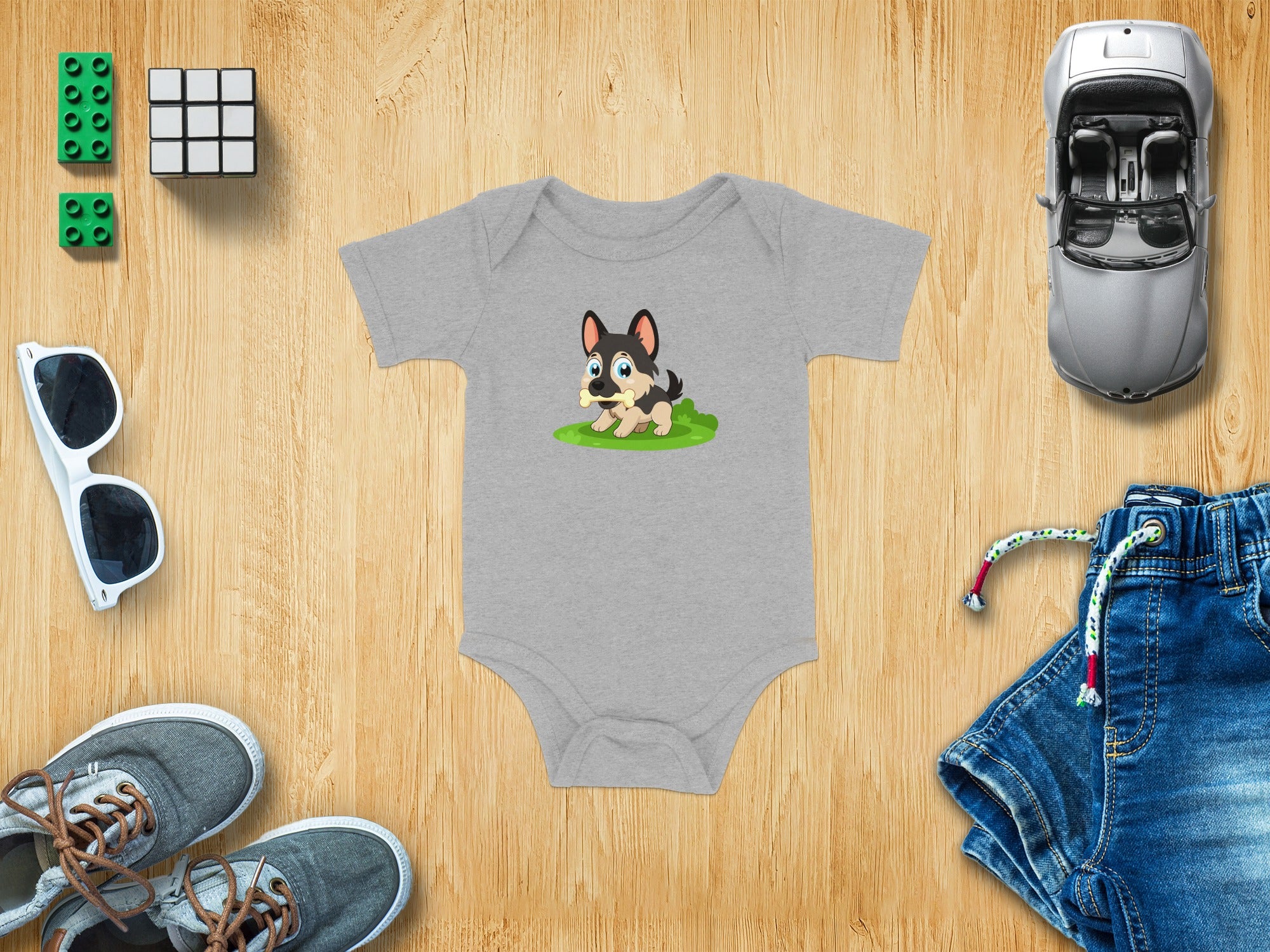 Gray baby onesie with cartoon dog holding bone, surrounded by toys and accessories.