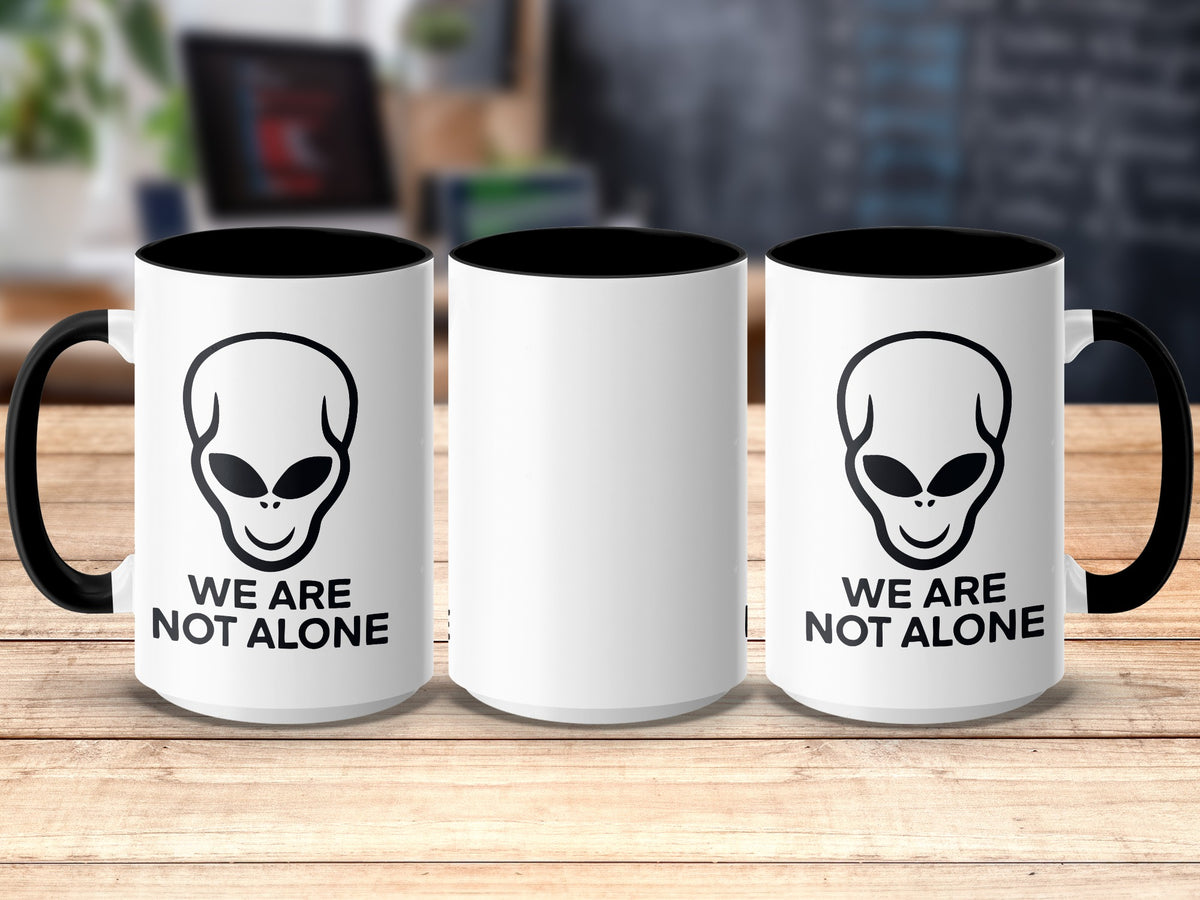 Three white mugs with black rims and handles, two featuring an alien graphic and "We Are Not Alone" text.