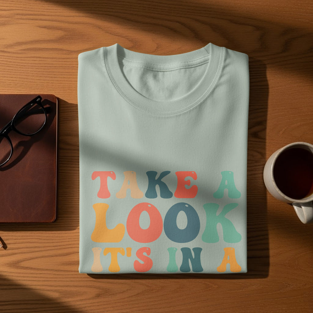 Light blue t-shirt with "TAKE A LOOK IT'S IN A" text in pastel colors.