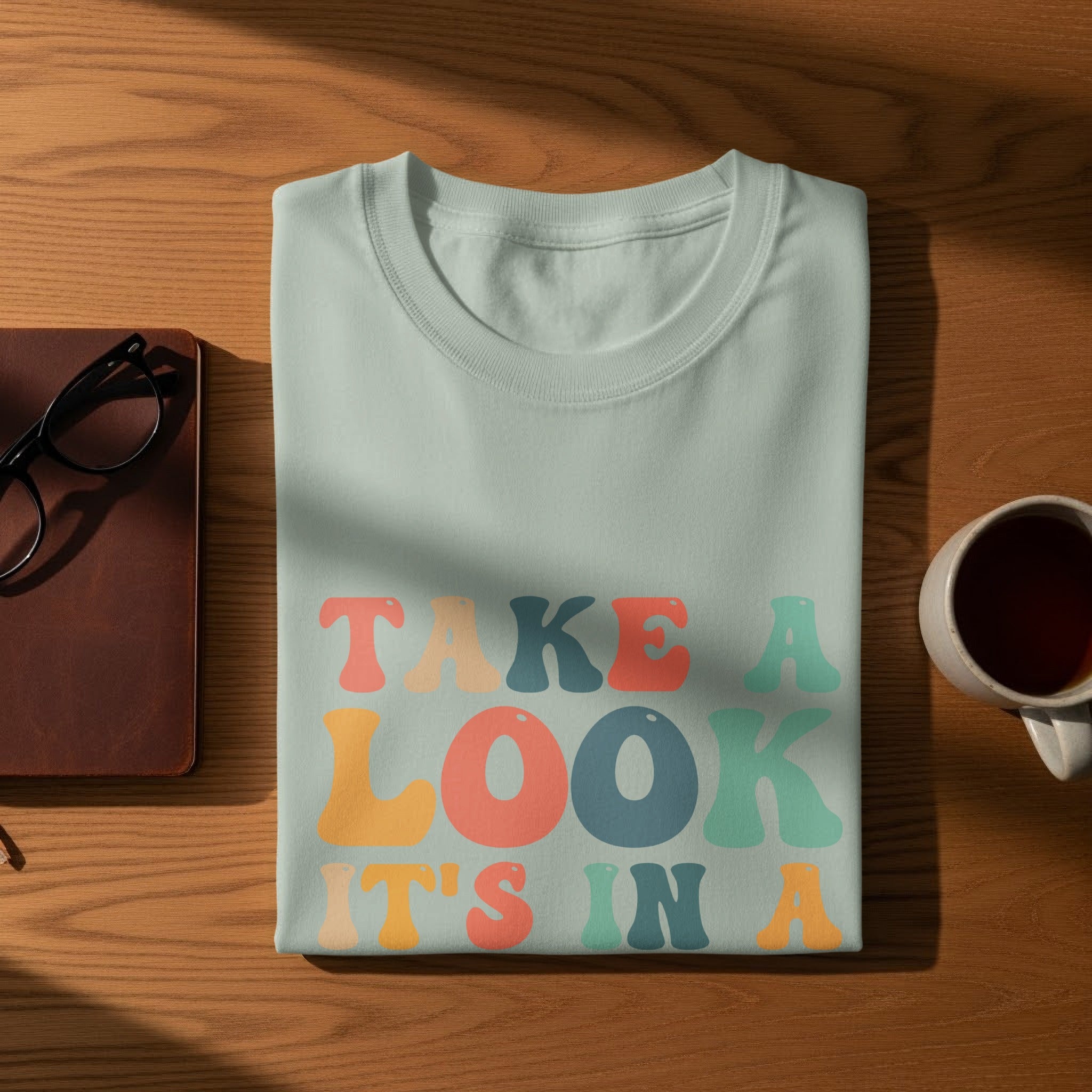 Light blue t-shirt with "TAKE A LOOK IT'S IN A" text in pastel colors.