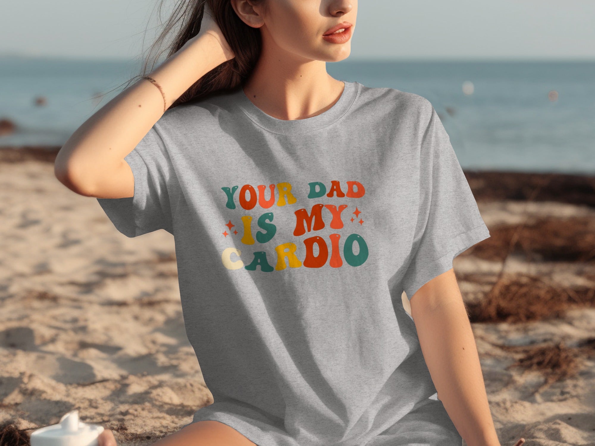 Grey t-shirt with "YOUR DAD IS MY CARDIO" text in colorful retro font.