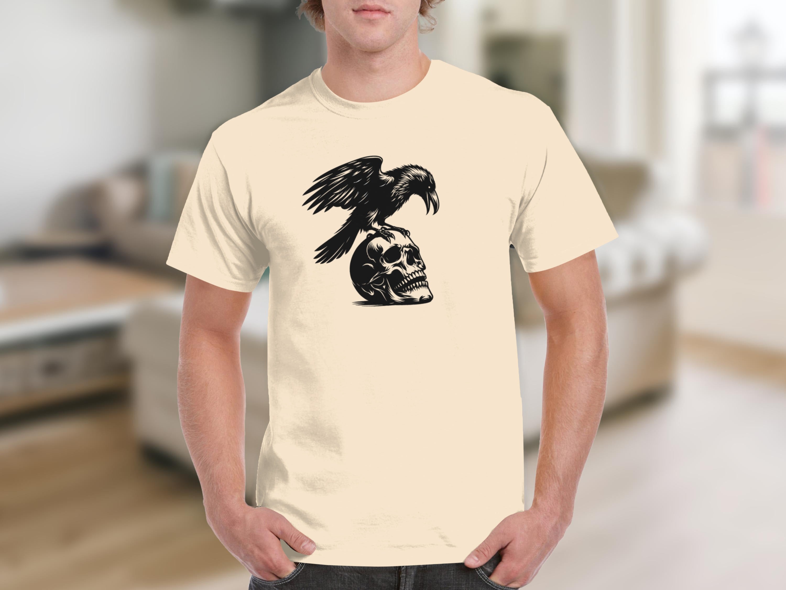 Black crow perched on a human skull graphic on a cream t-shirt.