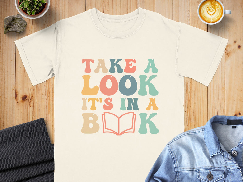 Cream t-shirt with "Take a look it's in a book" text and book graphic.