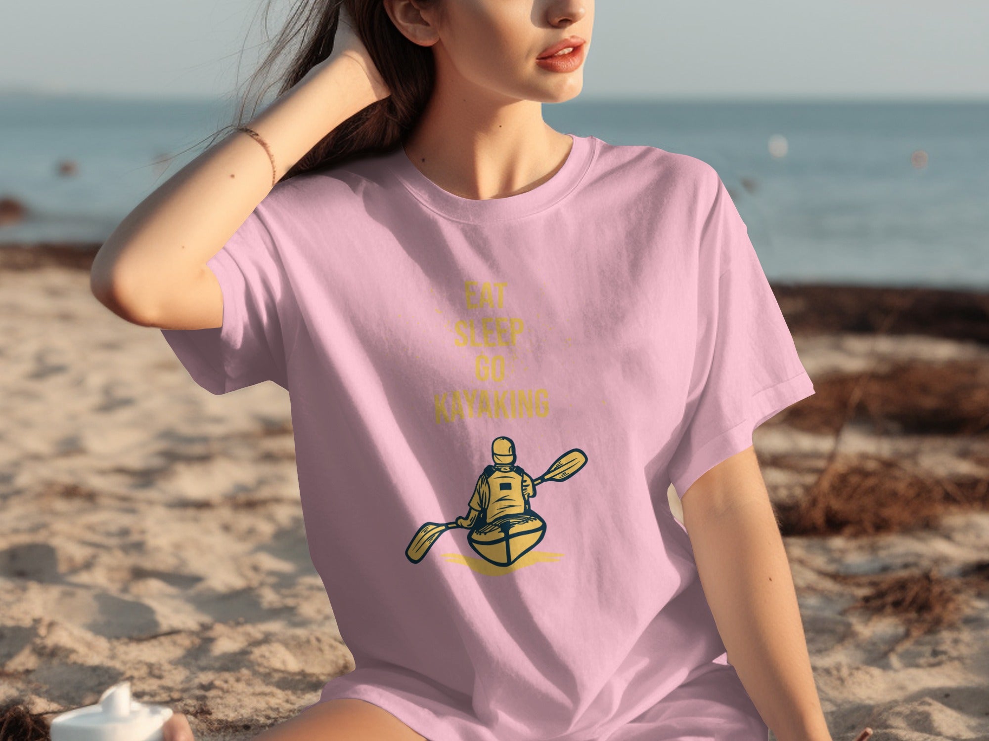 Pink t-shirt with yellow text and graphic of a kayaker paddling on water.