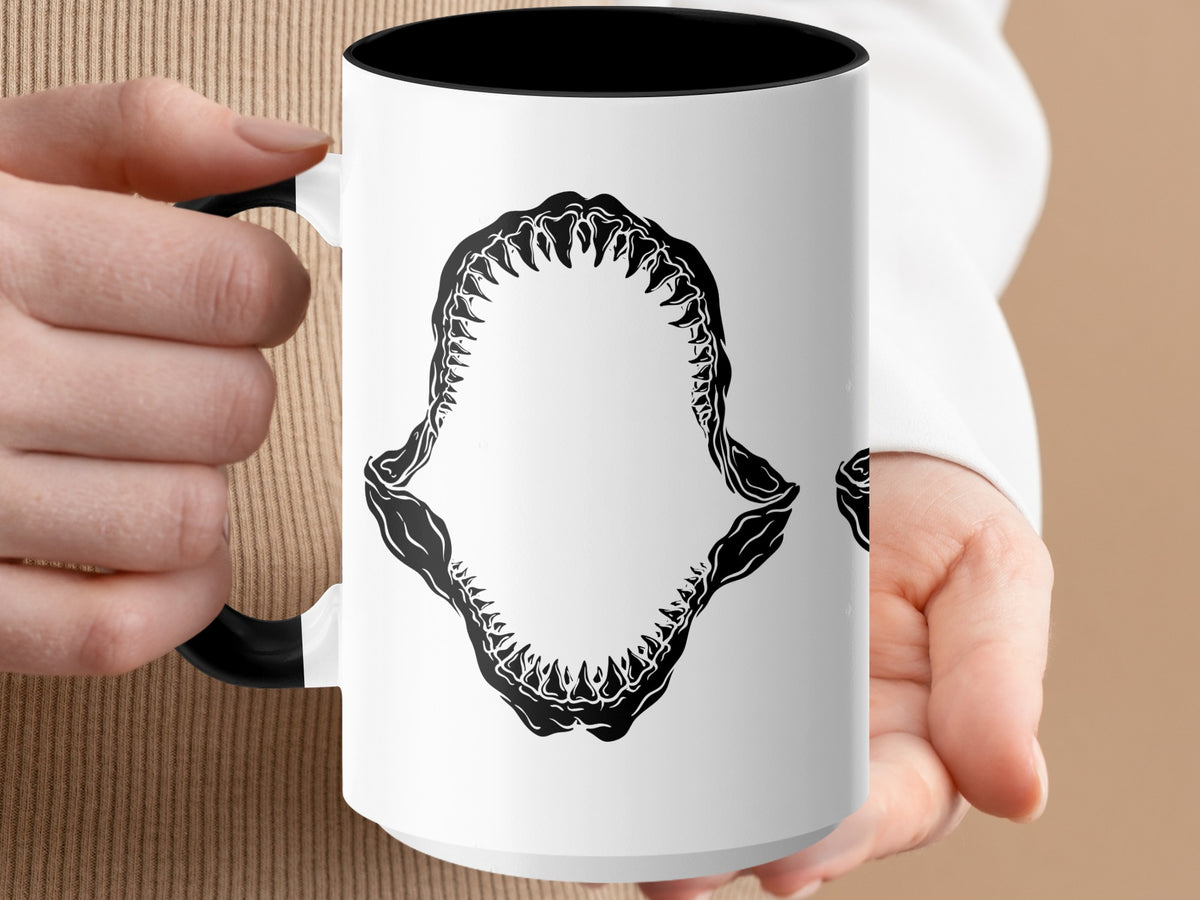 White mug with black shark jaw graphic and black handle held by a person.