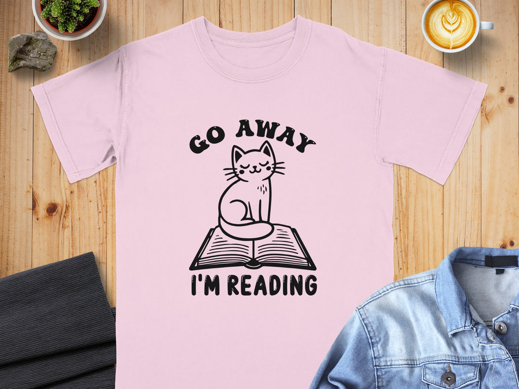 Pink t-shirt with black graphic of cat on book saying "GO AWAY I'M READING".