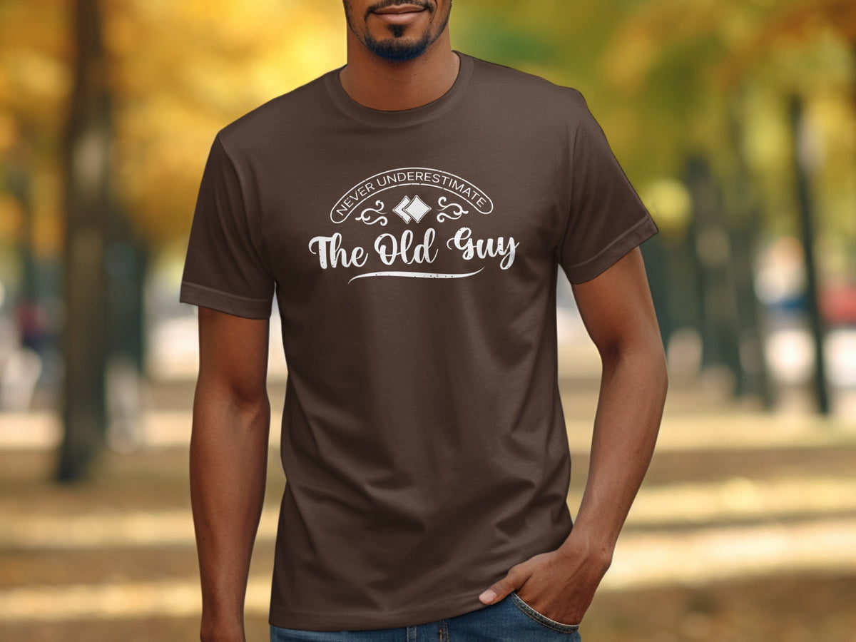 Brown t-shirt with white text "Never Underestimate The Old Guy" on the chest.