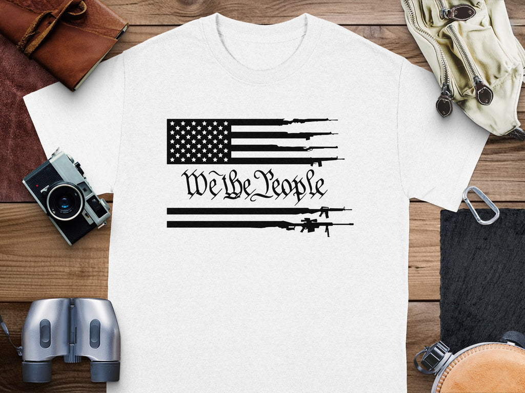 White t-shirt with black American flag design featuring guns and "We the People" text.