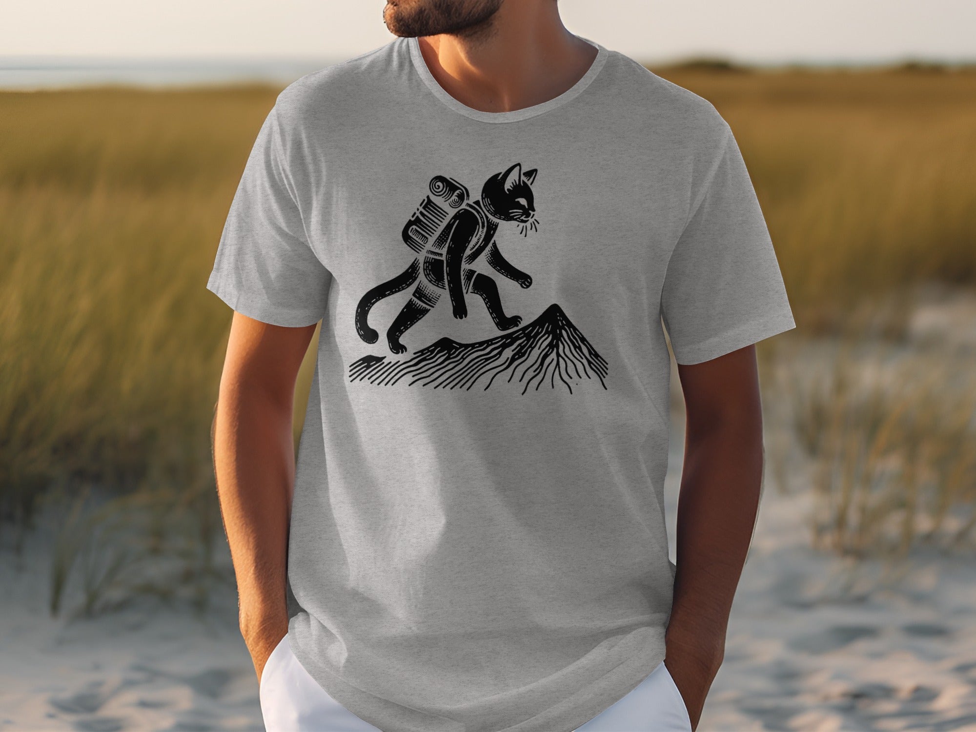 A black cat with a backpack hikes up a mountain on a gray t-shirt.