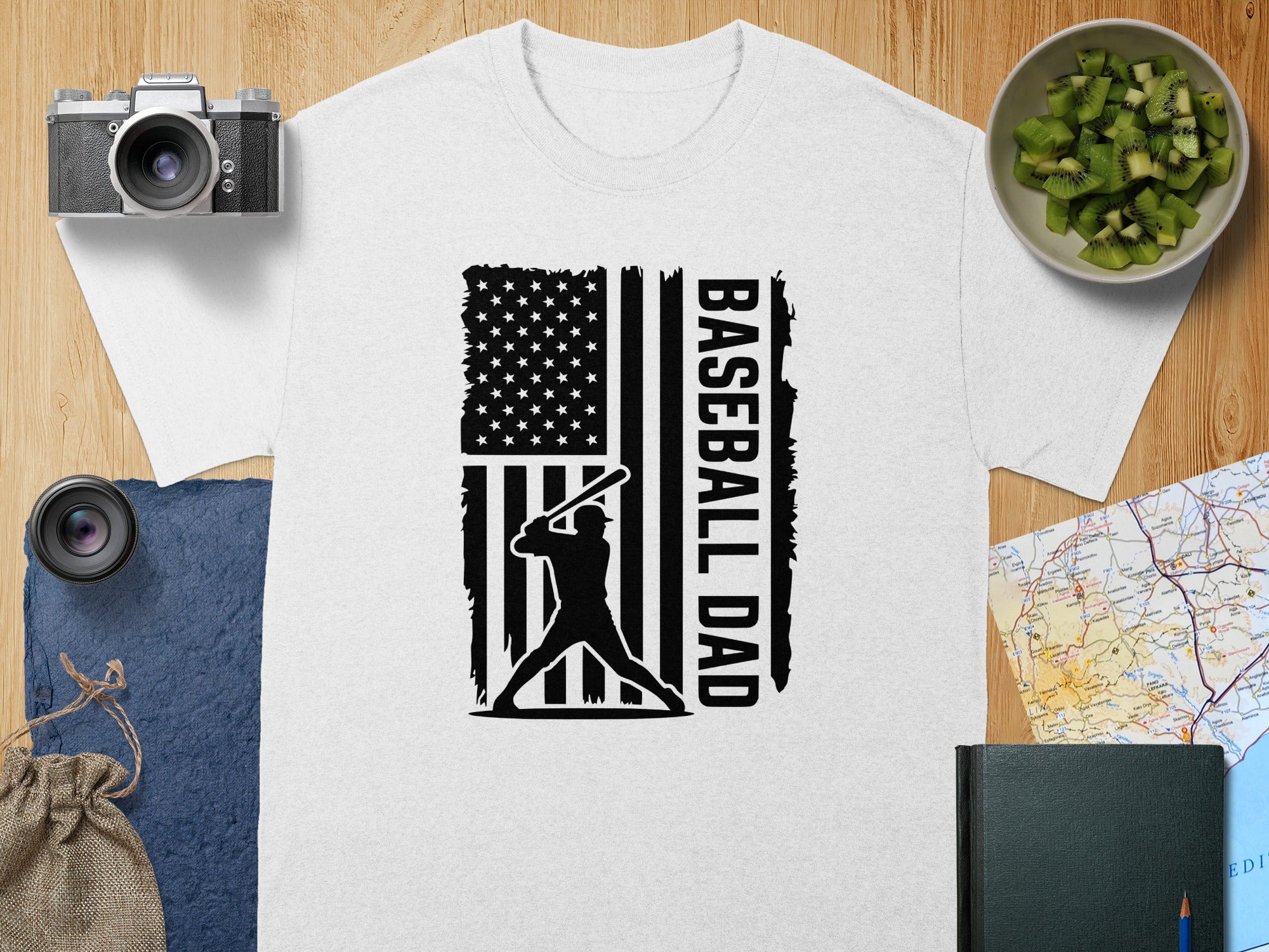 White t-shirt with black baseball player silhouette and American flag design reading "BASEBALL DAD".