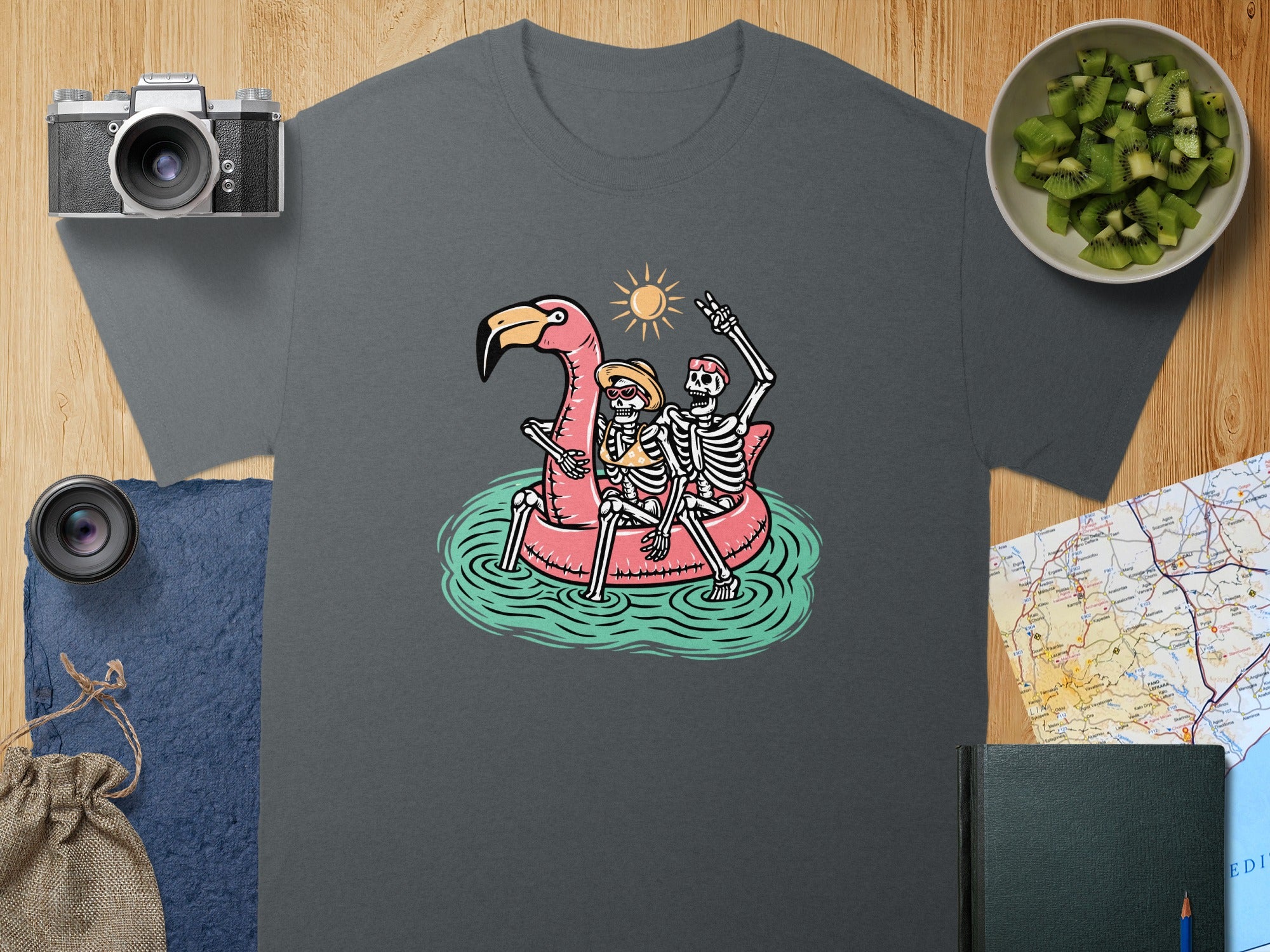 Skeletons on flamingo float with sun and waves, on a dark gray t-shirt.