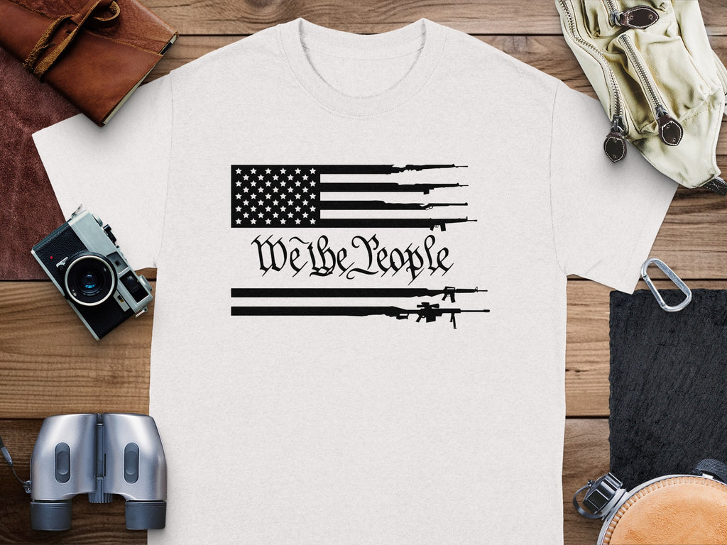 White t-shirt with American flag and guns graphic and "We the People" text.