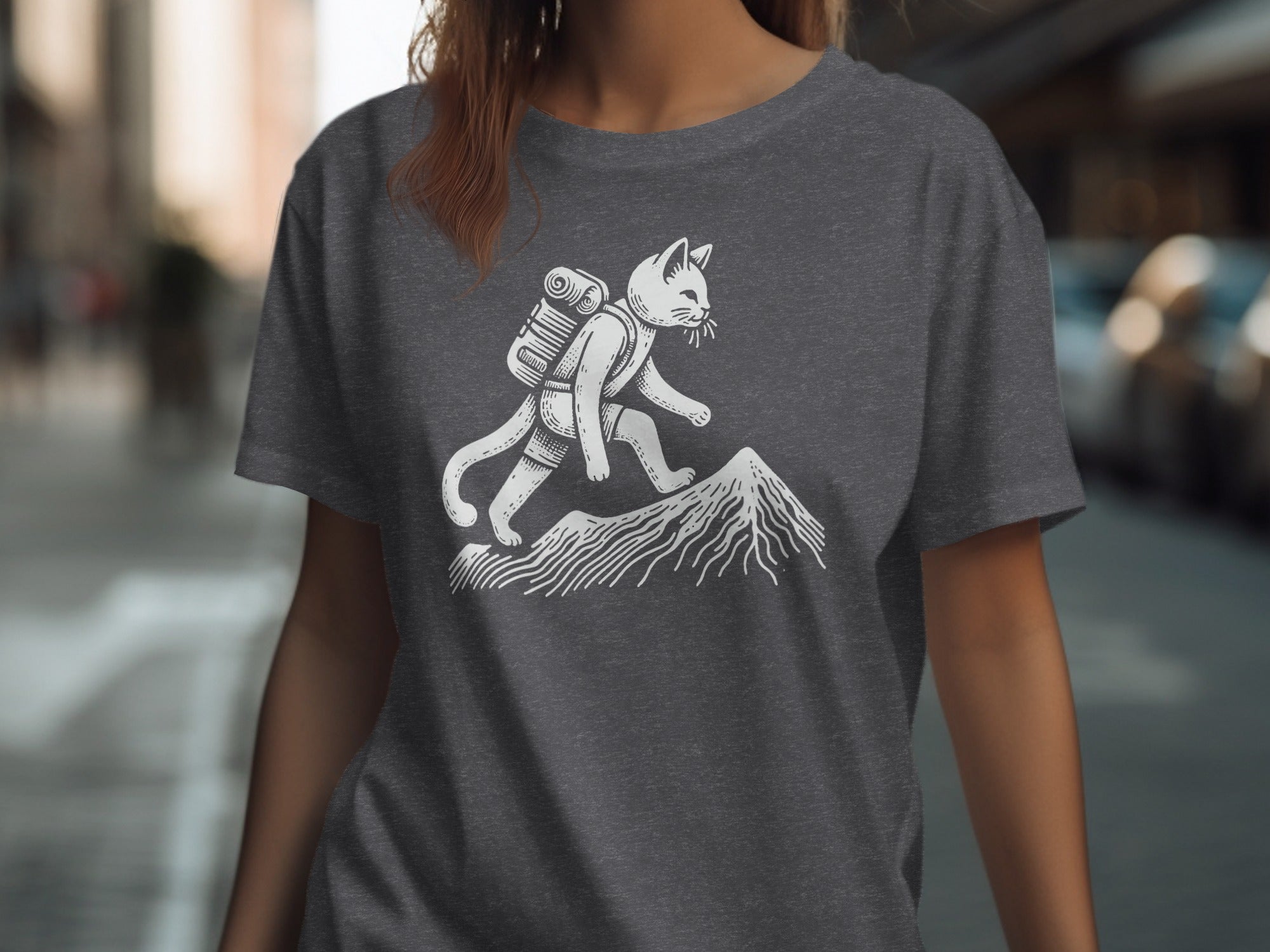 White illustration of a cat hiking up a mountain on a dark gray t-shirt.