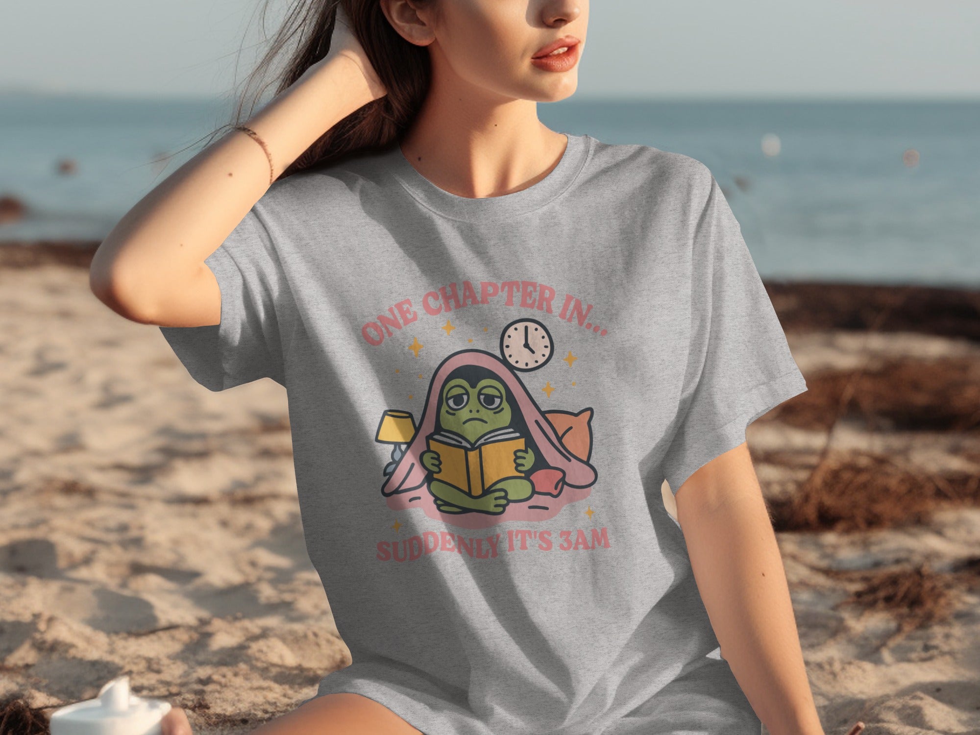 Grey t-shirt with graphic of frog reading a book "ONE CHAPTER IN... SUDDENLY IT'S 3AM".