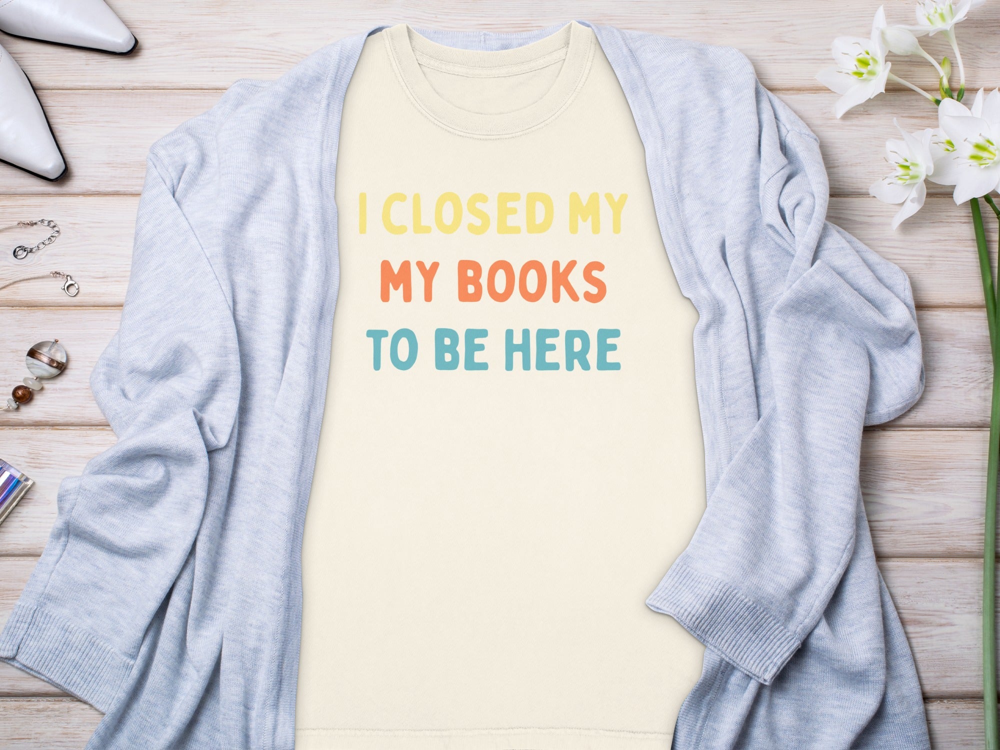 Cream t-shirt with yellow, orange, and blue text "I CLOSED MY MY BOOKS TO BE HERE".
