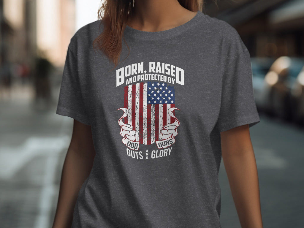 Dark gray t-shirt with American flag graphic and text "Born, Raised and Protected by God, Guns, Guts and Glory".