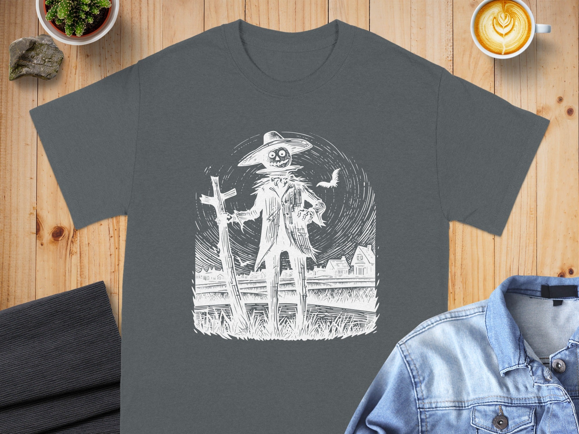 Dark gray t-shirt with white scarecrow, fence, and houses illustration.