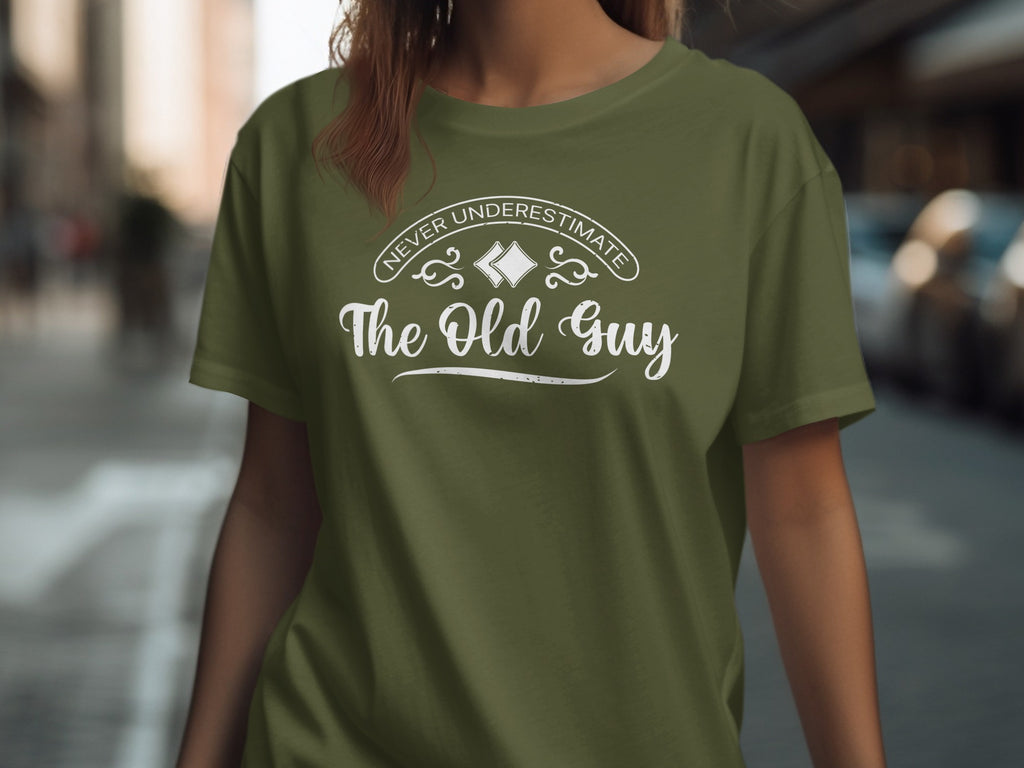Olive green t-shirt with white text "Never Underestimate The Old Guy".