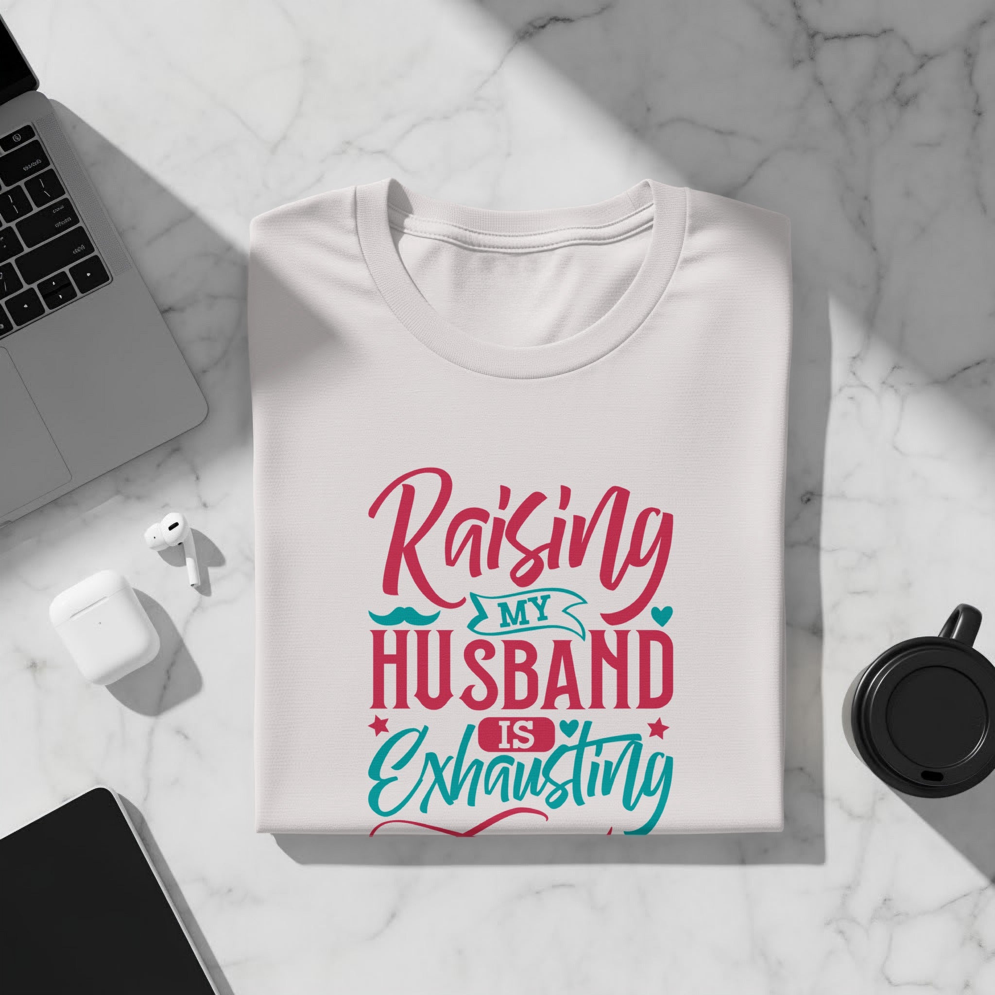 White t-shirt with "Raising my husband is exhausting" text in pink and teal.