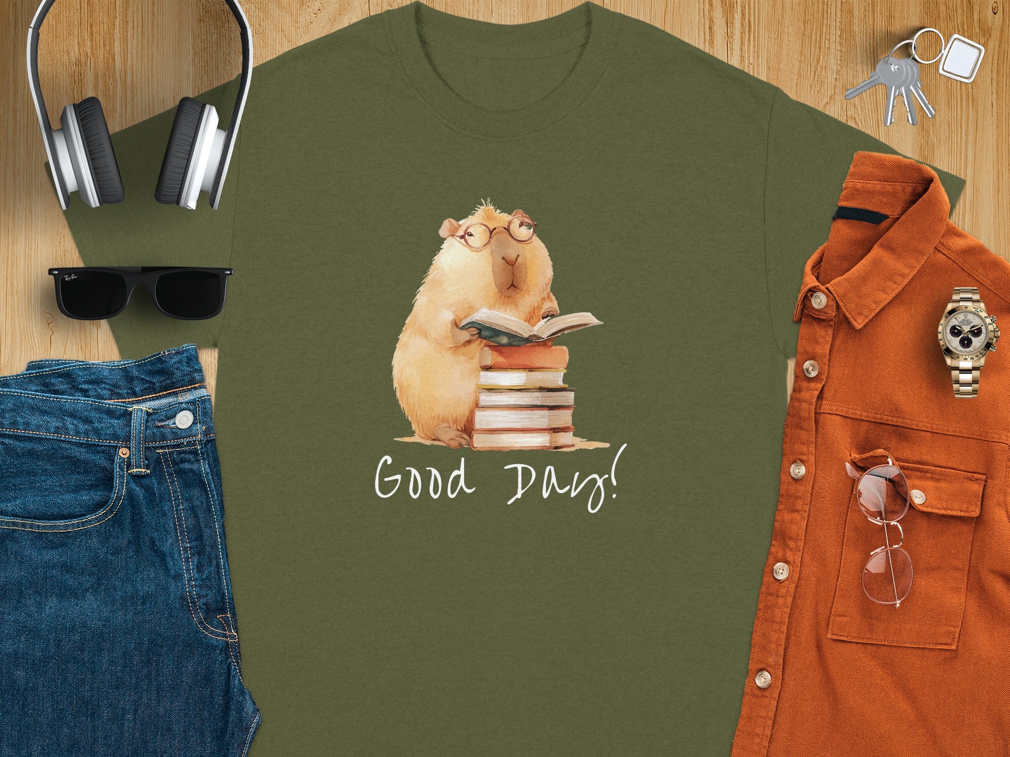 Olive green t-shirt with watercolor capybara reading a book on a stack of books, text reads "Good Day!".