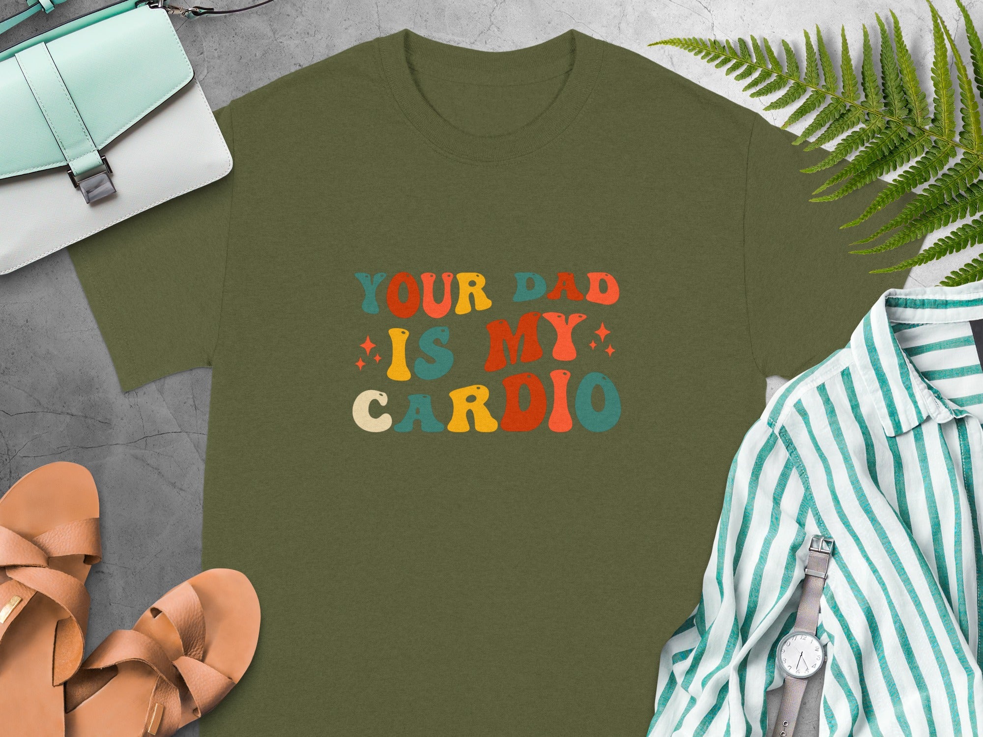 Olive green t-shirt with text "YOUR DAD IS MY CARDIO" in retro colorful font.