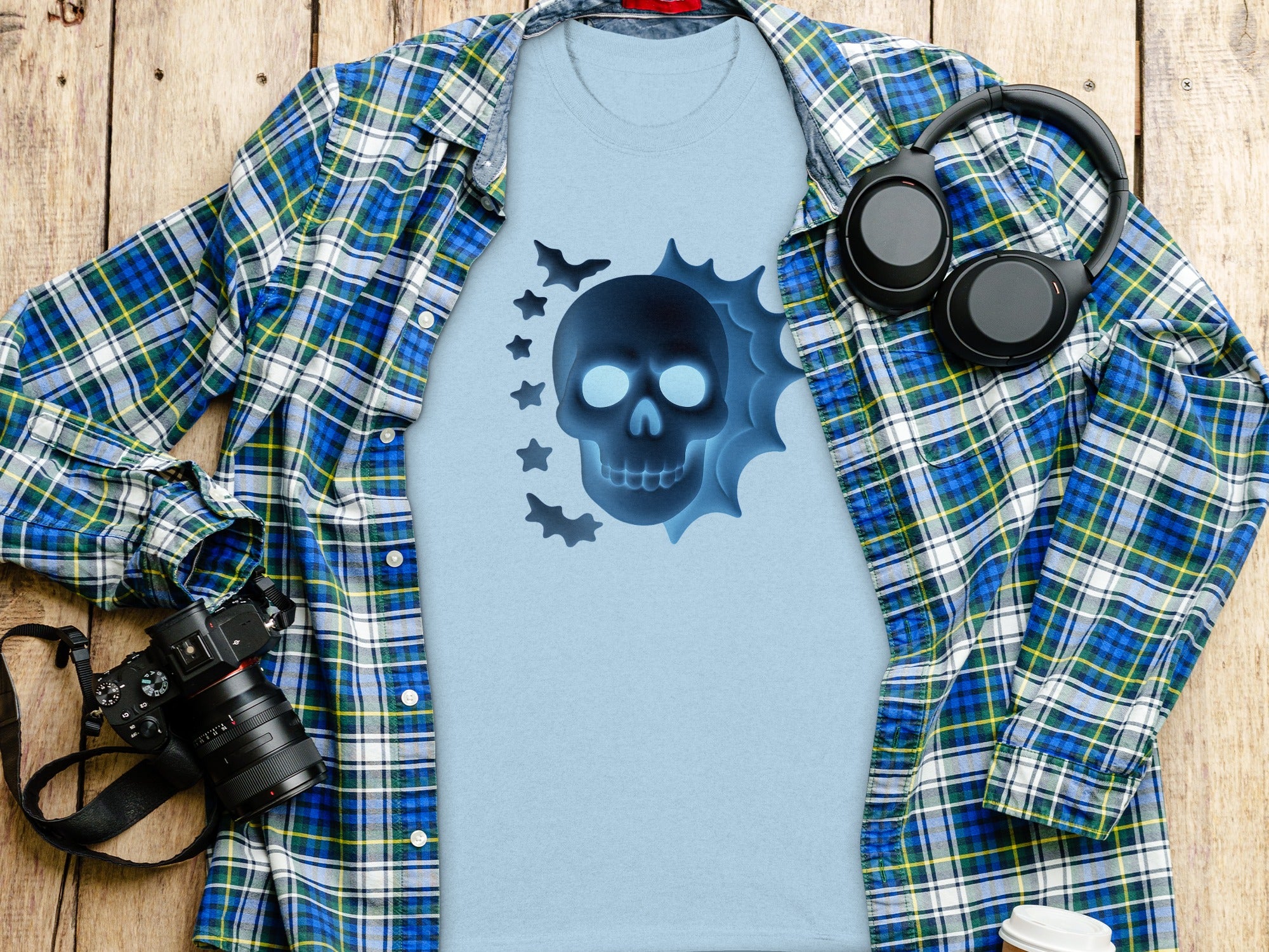 Light blue t-shirt with glowing blue skull and bat graphic, laid flat with open plaid shirt.