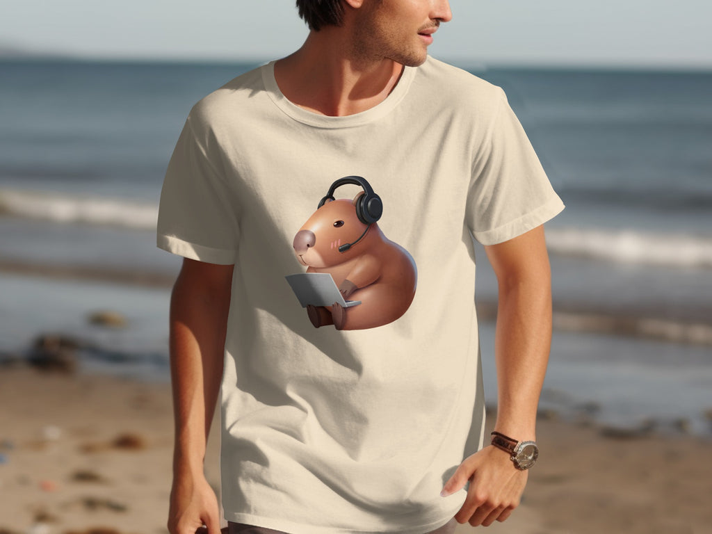 Cream t-shirt with a capybara wearing a headset and using a laptop, set against a beach backdrop.
