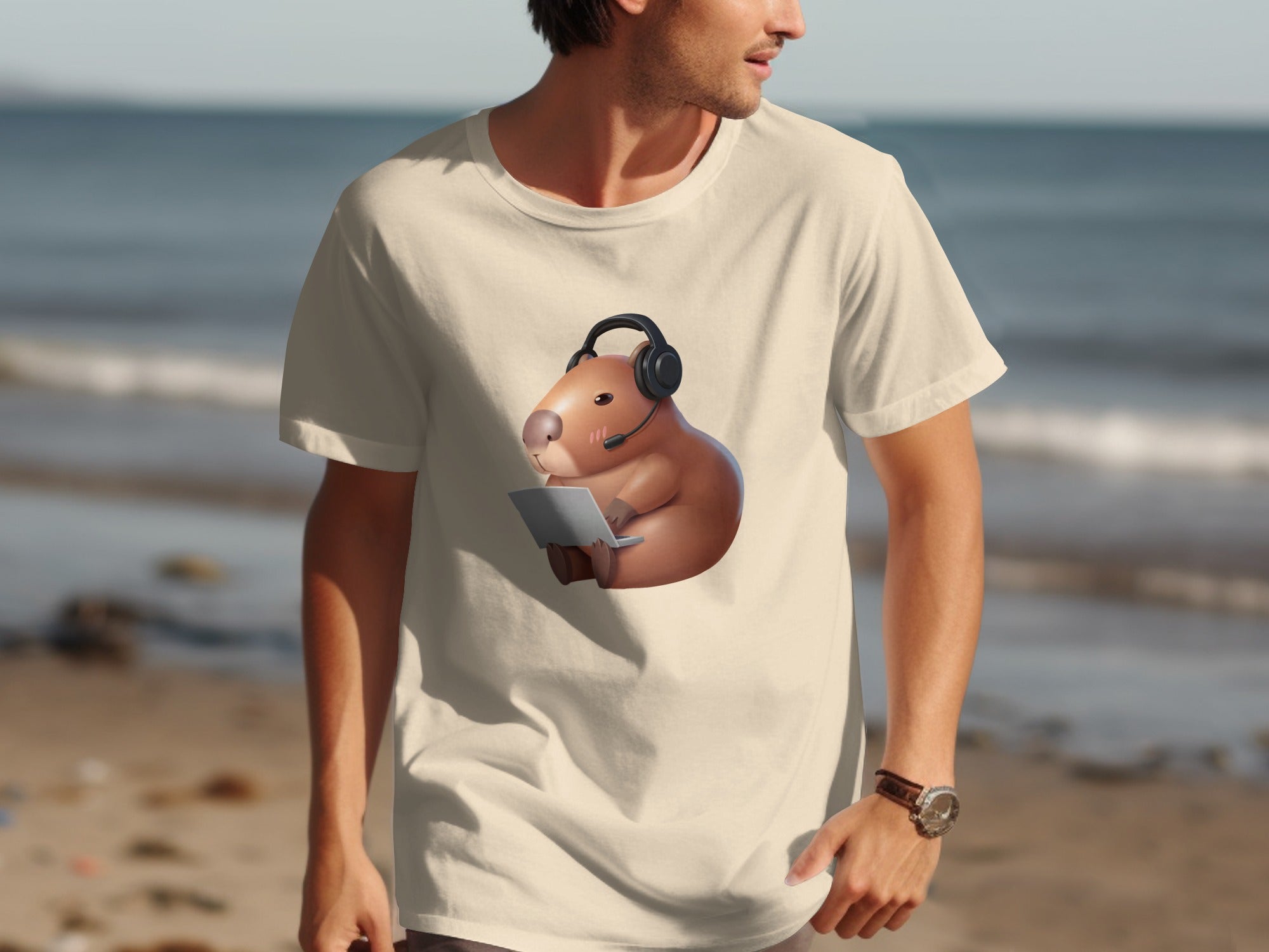 Cream t-shirt with a capybara wearing a headset and using a laptop, set against a beach backdrop.