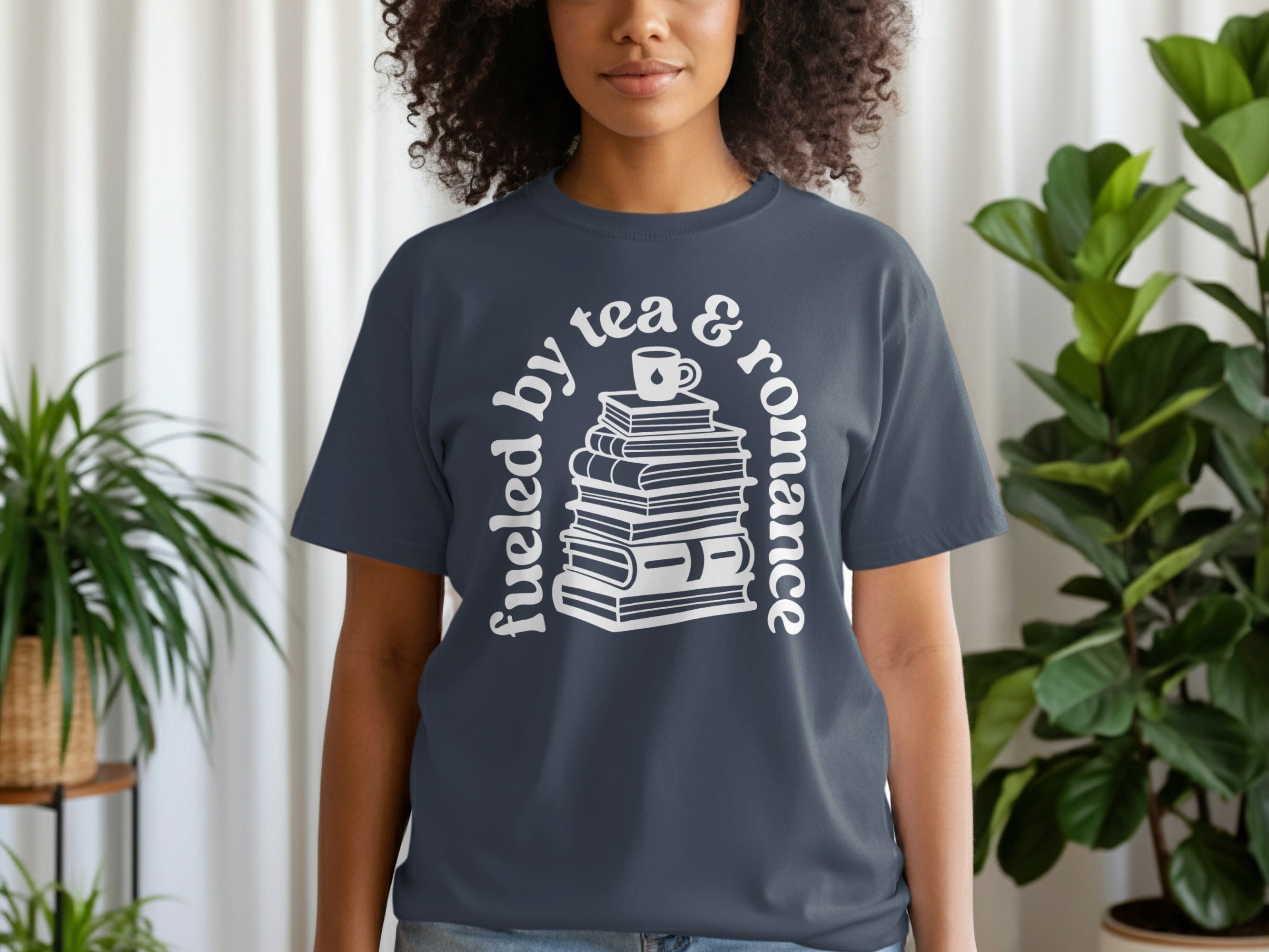 Dark blue t-shirt with white text "fueled by tea & romance" and stack of books graphic.